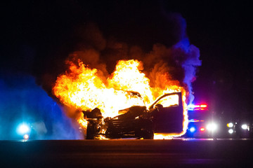 Car on fire at night with police lights in background
