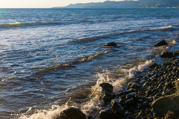 rocky sea shore with pebble beach, waves with foam
