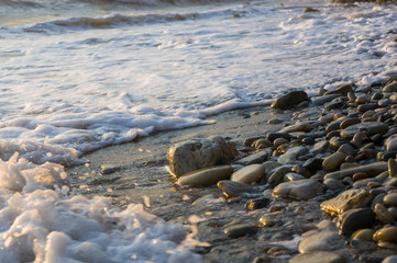 pebble stones on the sea beach, the rolling waves of the sea with foam