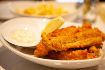 Pile of piping hot and crispy delicious Fish and chips or fried battered fish and hot potato fries served with tartar sauce.