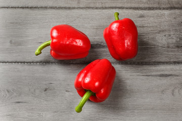 Tabletop view - three red bell peppers on rustic gray wood desk.