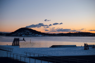Traveller man sitting on a pier and enjoying beautiful pink and orange sunset over the mountains and lake. Dusk. Norway