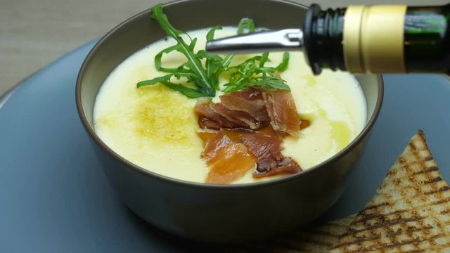 Restaurant dish, cheesy cream soup decorated with a sprig of arugula, toasted bacon with toast, the chief cook pours olive olive soup