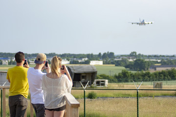 Young people taking photos of a Boeing 747 about to land