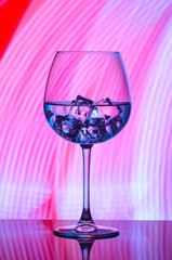 A glass with a drink and ice cubes on a red background with blue lights.