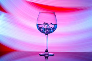 A glass with a drink and ice cubes on a red background with blue lights.