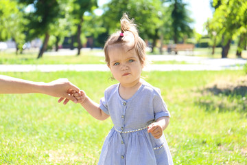 Adorable baby girl holding mother's hand while learning to walk outdoors