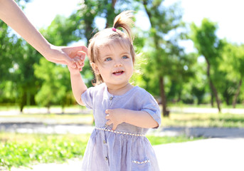 Adorable baby girl holding mother's hand while learning to walk outdoors