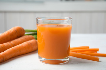 Glass with carrot juice and fresh vegetable on table