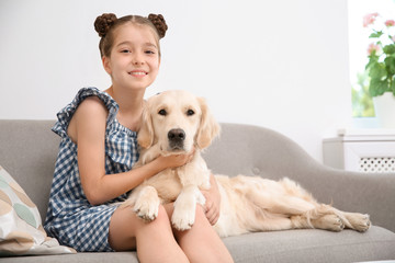 Cute little child with her pet on sofa at home