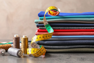 Bobbins with threads, measuring tape and stack of colorful fabrics on table. Tailoring accessories