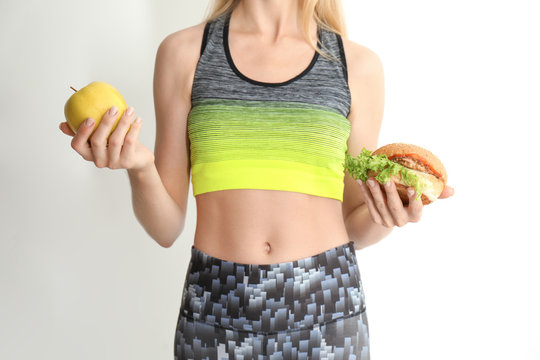 Woman holding tasty sandwich and fresh apple on light background. Choice between diet and unhealthy food