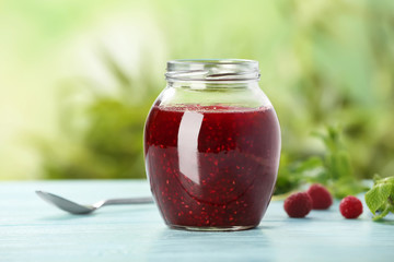 Jar with delicious raspberry jam on table against blurred background