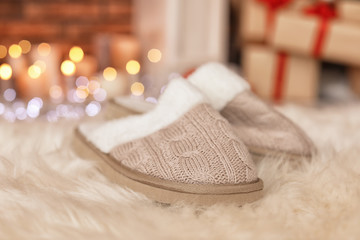 Fototapeta na wymiar Soft slippers, fuzzy rug and blurred Christmas lights on background