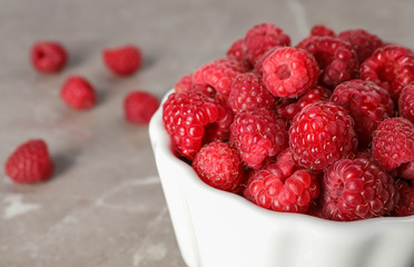 Bowl with ripe aromatic raspberries on table