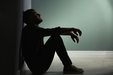 Depressed young man sitting on floor in darkness - Powered by Adobe