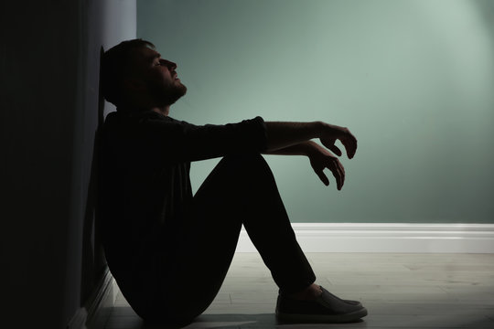 Depressed young man sitting on floor in darkness