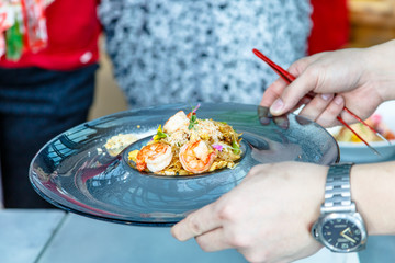 The chef prepares a dish of prawn noodles and decorates it with edible flowers.