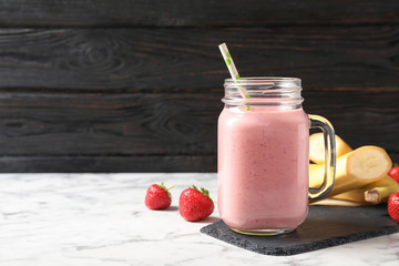 Mason jar with tasty strawberry smoothie on marble table