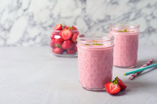 Glass jars with tasty strawberry smoothie on table