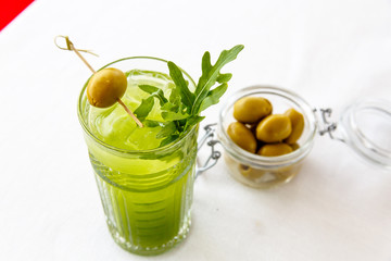 Lemonade from arugula in a glass and olives in a jar are on the table