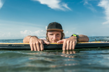 portrait of male surfer resting in ocean with surfing board and looking at camera at Nusa Dua Beach, Bali, Indonesia