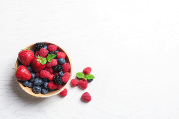 Bowl with raspberries and different berries on wooden table, top view