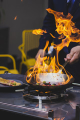 Chef doing flambe to food in pan with alcohol in big flame