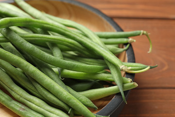 Plate with fresh green French beans on wooden table, closeup