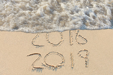 New Year's Day 2019 sign in beach sand with frothy surf
