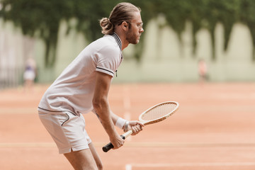 side view of handsome tennis player ready for game with racket at tennis court
