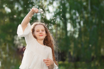 Curly girl dancing in flying dandelions outdoors.
