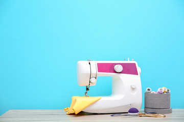 Sewing machine on table against color background