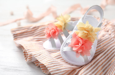 Pair of cute baby sandals and clothes on table