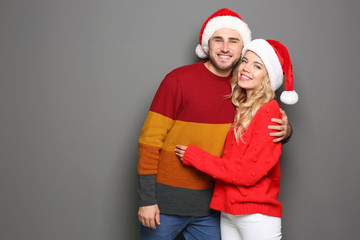Young couple in Santa hats on grey background. Christmas celebration