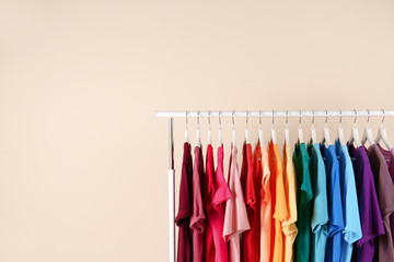 Many t-shirts hanging in order of rainbow colors on light background
