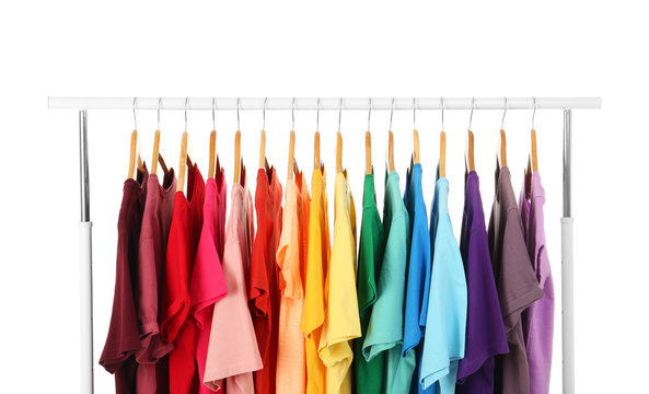 Many t-shirts hanging in order of rainbow colors on white background