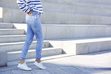 Young hipster woman in stylish jeans standing near stairs outdoors