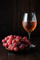 Glass of pink wine and red grapes on dark background