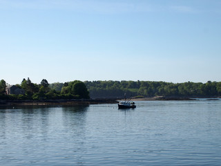 Fototapeta na wymiar Fishing boat rests in water of Casco Bay off shore of island with house and trees