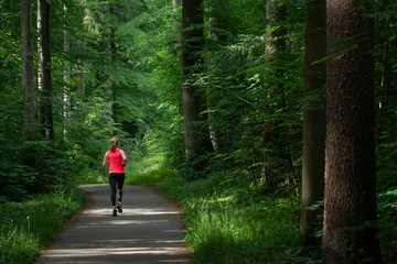 Young woman running along path through green forest. - 213128233