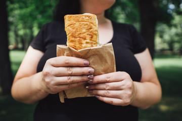Unhealthy fattening food,high-calorie snack, eating on the go, take-out meals. Overweight woman eating shawarma walking in the street