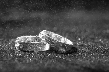 Two wedding rings with water drops on black background with copy space.