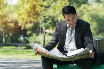 Businessman reading newspaper and looking for new job in public park with copy space.
