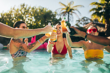 Group of friends toasting beers in swimming pool party