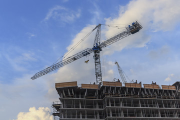 Cranes on a construction site with a blue and cloudy sky in the background