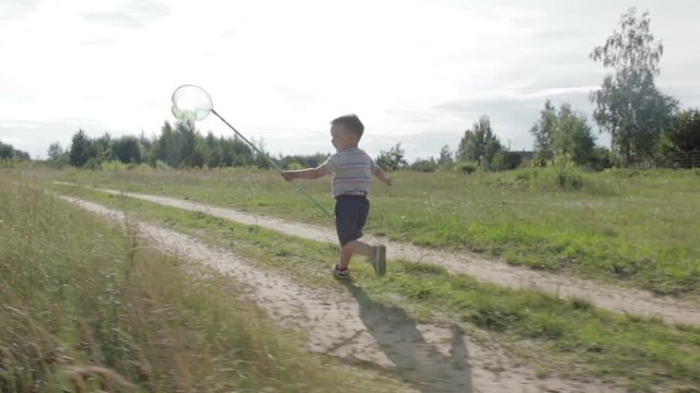 Cheerful little boy in shorts and a t-shirt, running on the lawn and catching a butterfly green net.