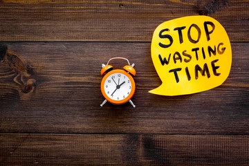 Stop wasting time hand letterng in cloud near alarm clock on dark wooden background top view copy space. Business concept, motivation