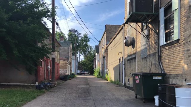 A daytime summer establishing shot of an empty alley in a small rust belt Ohio valley town. Pittsburgh suburbs.  	