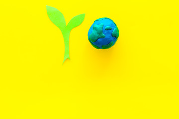 Planet, ecology. plastiline symbol of planet Earth globe and plant coutout on yellow background top view copy space